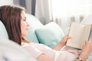 Young woman lying on couch and reading a book at home, casual style indoor shoot